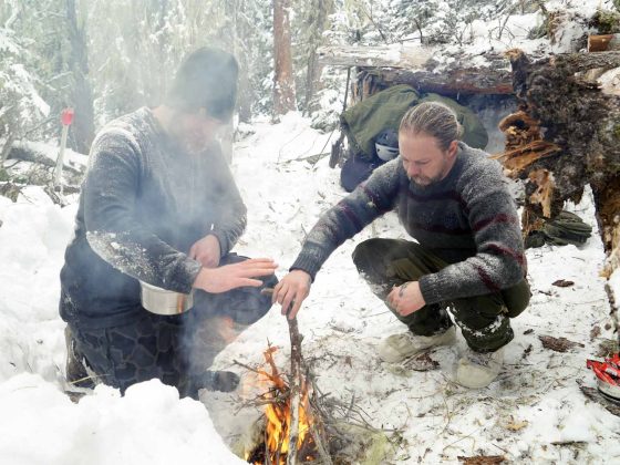 Two men tending a fire in snowy forest.
