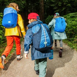 Kids wearing mec backpacks walking on a road