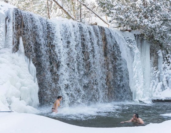 Two people swimming below a waterfall in winter in Ontario, Hoggs Falls