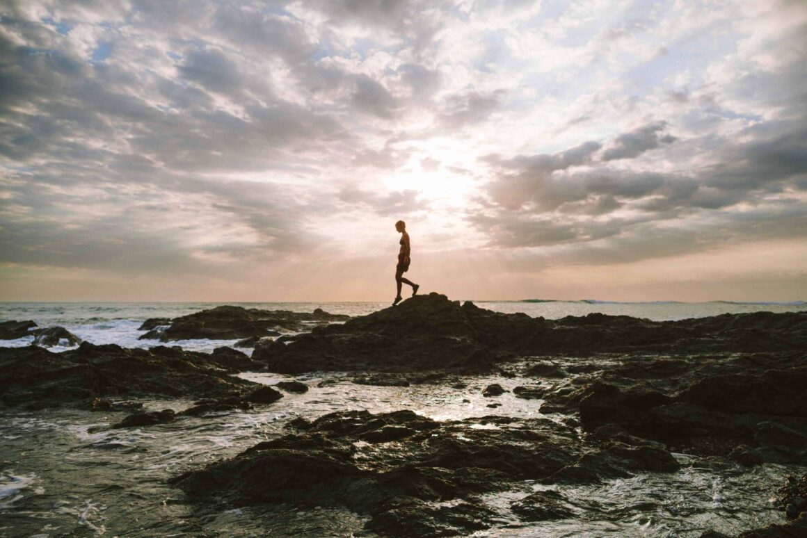 Angel Collinson walking on a rocky beach at sunset
