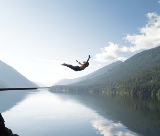Woman diving off cliff into lake in the Coast Mountains BC